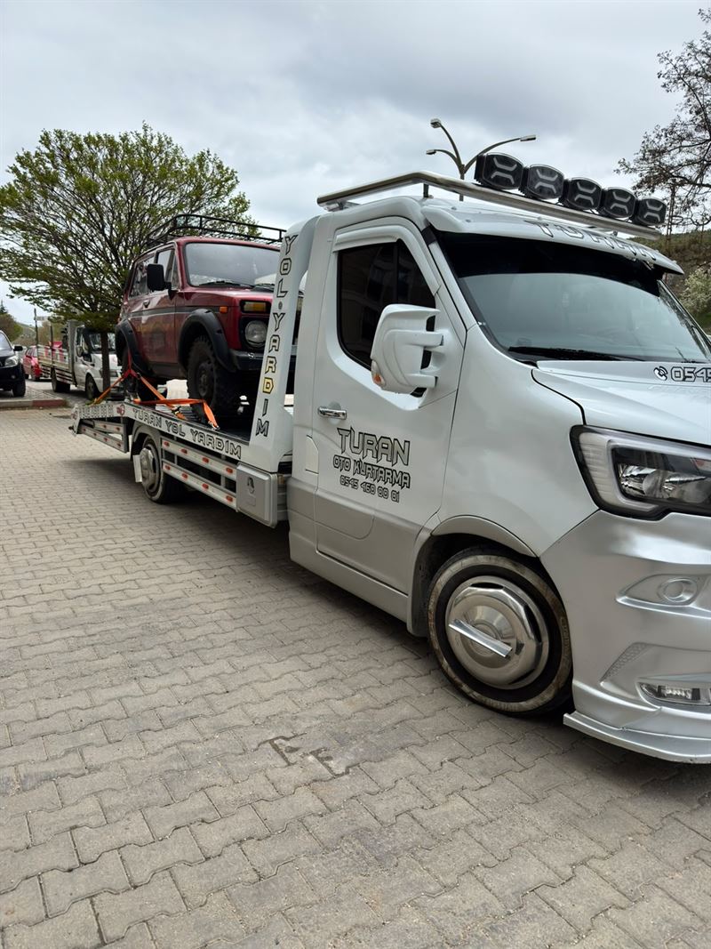 Koyu kırmızı pickup aracının ağaçlı yolda çekiciye yüklenmesi